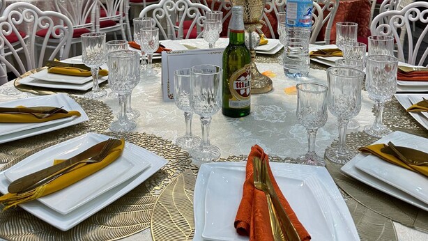 Un salón de banquetes con mesas redondas dispuestas para cenar, con sillas blancas y detalles dorados.