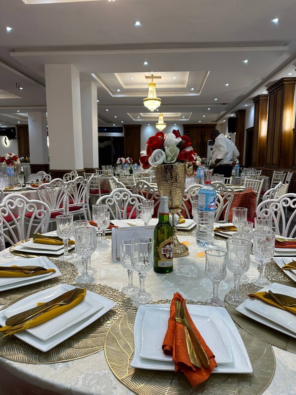 A banquet hall with round tables set for dining, featuring white chairs and gold accents.
