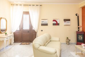 A living room with a beige sofa, a wooden door with curtains, a small table with a vase, and a heater. - Casa del Sole - Menfi (Menfi)