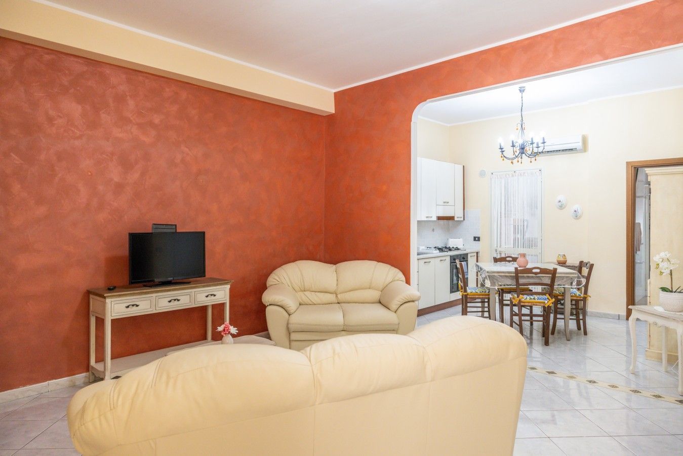 Uma sala de estar com sofá, televisão sobre uma mesinha de apoio e um espaço de refeições com mesa e cadeiras.