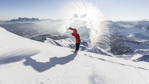 Una persona con chaqueta roja de pie sobre una montaña nevada bajo un cielo despejado.