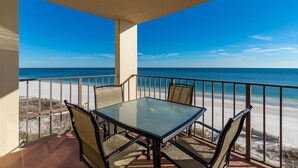 A balcony with a glass table and chairs, overlooking a beach with a clear blue sky. - Phoenix Iii 3073 1 Bedroom Condo (Orange Beach)