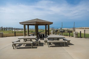 Un patio al aire libre con mesas de picnic y un pabellón, con vistas a la playa.