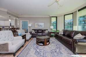 A spacious living room with a large window, a fireplace, and a dining area. - Phoenix On The Bay 1315 3 Bedroom Condo (Orange Beach)