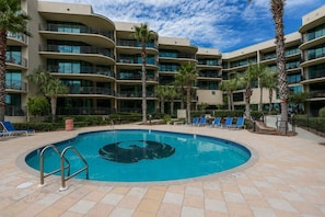 Ein Hotel mit einem kreisförmigen Pool, mehreren Balkonen und Palmen.