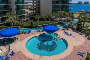 A rooftop pool with blue umbrellas, lounge chairs, and a view of the ocean. - Phoenix On The Bay 1315 3 Bedroom Condo (Orange Beach)