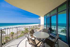 A balcony with a table and chairs, overlooking a beach with umbrellas and the ocean. - Phoenix West 405 3 Bedroom Condo (Orange Beach)
