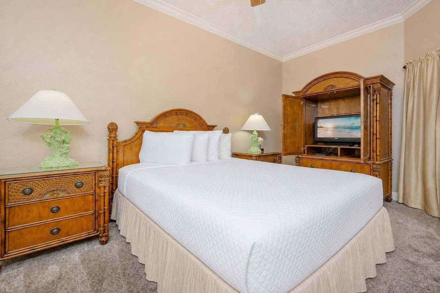 A hotel room with a large bed, wooden headboard, two bedside tables with lamps, a television, and a wardrobe.