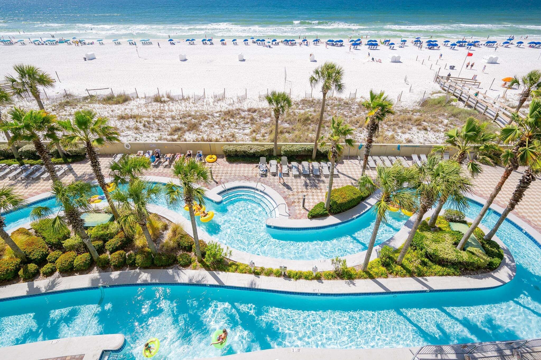 A resort with a pool area, beach, and palm trees.