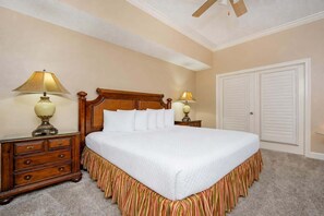 A neatly made bed with a wooden headboard, two bedside tables with lamps, a large closet, and a ceiling fan. - Phoenix West 405 3 Bedroom Condo (Orange Beach)