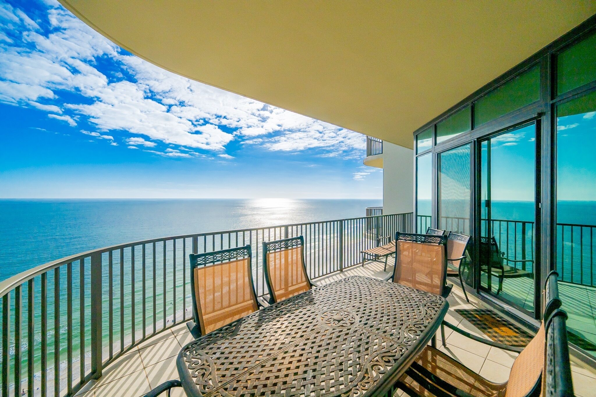A balcony with a table and chairs, overlooking a beach and the sea.