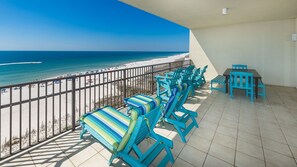 A balcony with a view of the beach, equipped with blue chairs and a table. - Phoenix West 709 4 Bedroom Condo (Orange Beach)