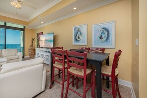 A dining area with a table and chairs, a television, and artwork on the wall. - Phoenix West 709 4 Bedroom Condo (Orange Beach)
