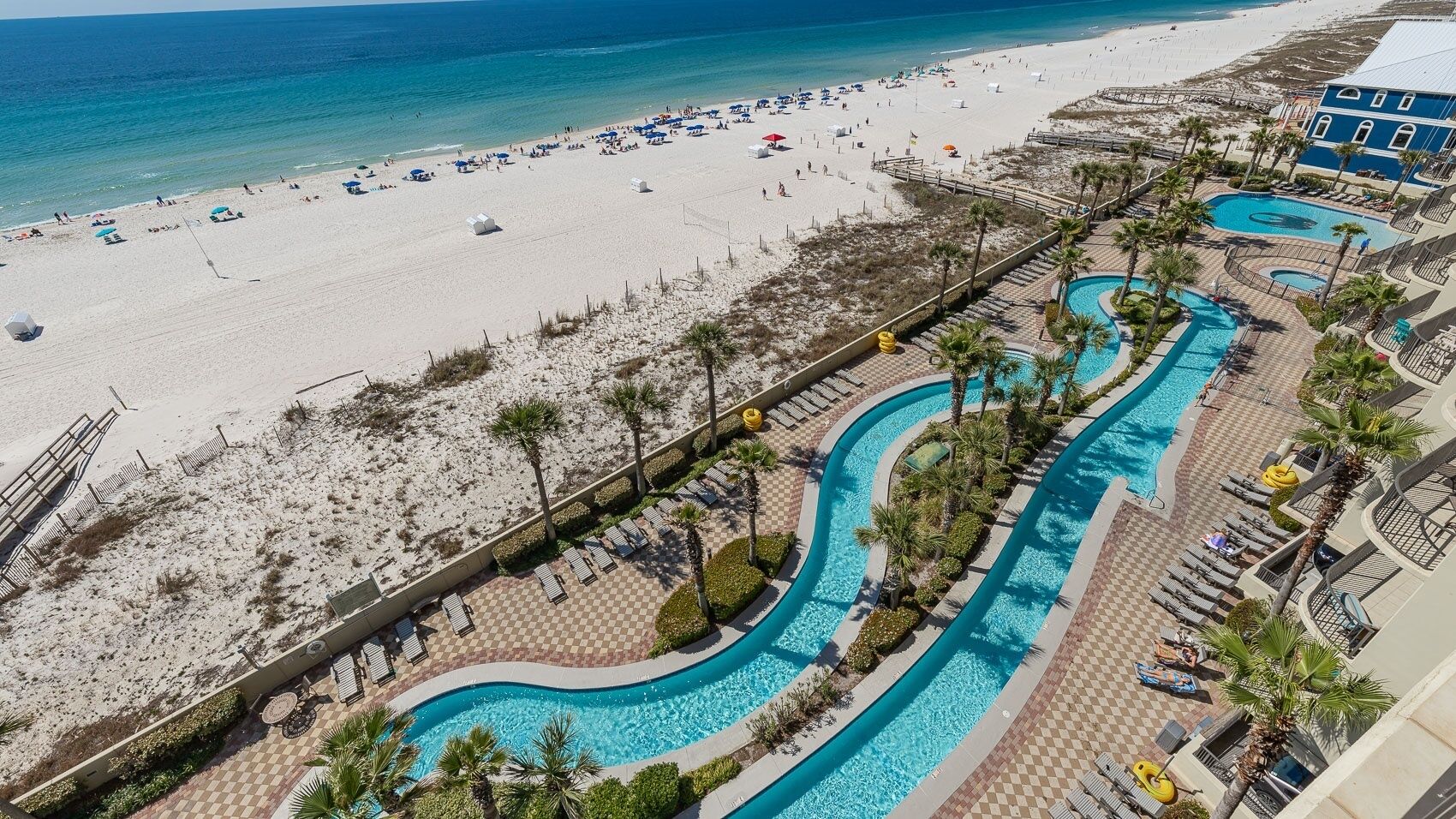 Un complexe hôtelier doté d’une plage, d’un espace piscine et d’un bâtiment à la façade bleue.