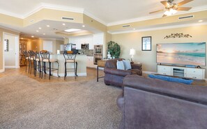A spacious living area with a kitchen, dining area, and a large flat-screen TV. - Phoenix West 1701 4 Bedroom Condo (Orange Beach)