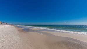 A beach with a clear sky, sandy shore, and a few buildings in the background. - Phoenix West 1701 4 Bedroom Condo (Orange Beach)