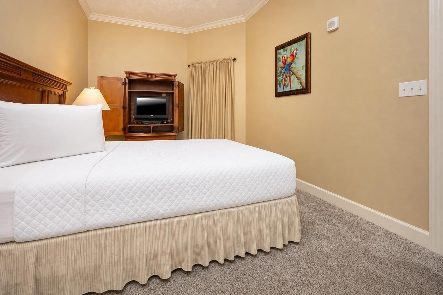 A hotel room with a bed, a television, a painting, and a carpeted floor.