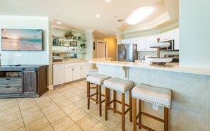 A kitchen with a bar area, white cabinets, and a tiled floor. - Phoenix West 602 3 Bedroom Condo (Orange Beach)