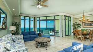 A spacious living room with a view of the ocean, furnished with blue sofas and a wooden coffee table. - Phoenix West 602 3 Bedroom Condo (Orange Beach)