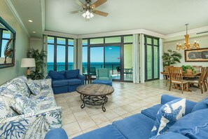 A spacious living room with a view of the ocean, furnished with blue sofas and a wooden coffee table. - Phoenix West 602 3 Bedroom Condo (Orange Beach)