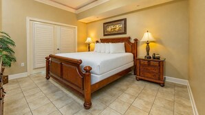 A bedroom with a wooden bed, two bedside tables with lamps, a ceiling fan, and a door with a view of the outside. - Phoenix West 602 3 Bedroom Condo (Orange Beach)