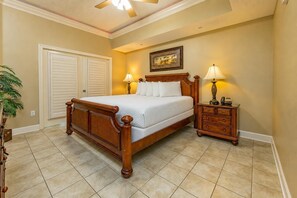 A bedroom with a wooden bed, two bedside tables with lamps, a ceiling fan, and a door with a view of the outside. - Phoenix West 602 3 Bedroom Condo (Orange Beach)
