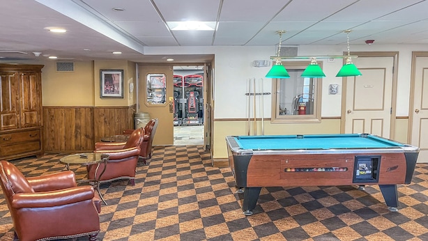 Een pooltafel met een geruit vloerkleed, leren stoelen en een biljarthouder.
