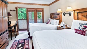 Een hotelkamer met twee bedden, een bureau, een stoel, een lamp en uitzicht op groen buiten.