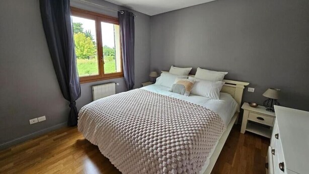 Quarto com uma cama grande, mesa de cabeceira, cômoda e uma janela com cortinas.