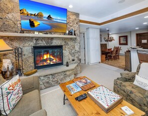 A living room with a stone fireplace, a flat-screen TV mounted on the wall, and a Scrabble game on the coffee table. - Ski-In/Out Beaver Creek Condo w/Amenities (Beaver Creek)