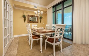 A dining area with a table and chairs, a chandelier, a large mirror, and a view through a glass door. - Phoenix West 2606 3 Bedroom Condo (Orange Beach)