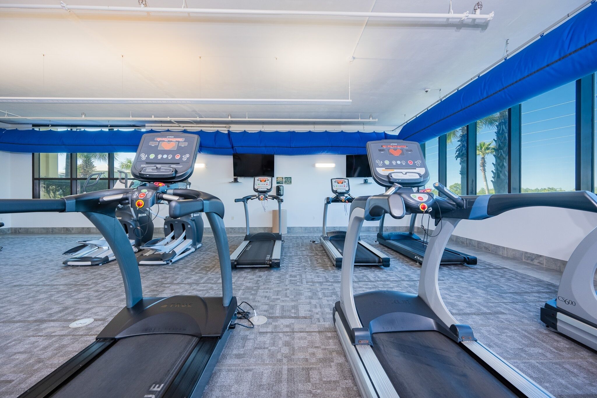 Un gimnasio con cintas de correr, bicicletas estáticas y una banca para pesas.