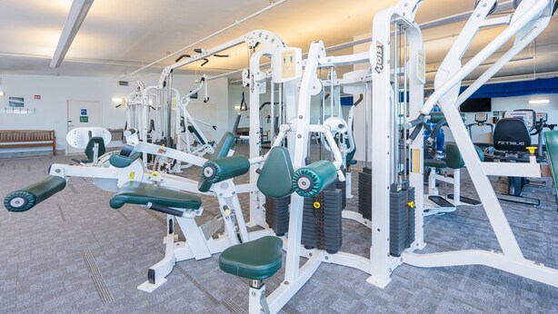 Ett gym med olika träningsmaskiner, en bänk och en vägg full med speglar.