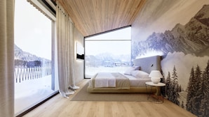 A modern bedroom with a large window, a bed, a bedside table, and a wall mural of mountains. - Superior Apartment # B8 with 3 bedrooms and sauna (Söll)