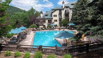 A swimming pool surrounded by lounge chairs and umbrellas, with a stone wall and a wooden fence.