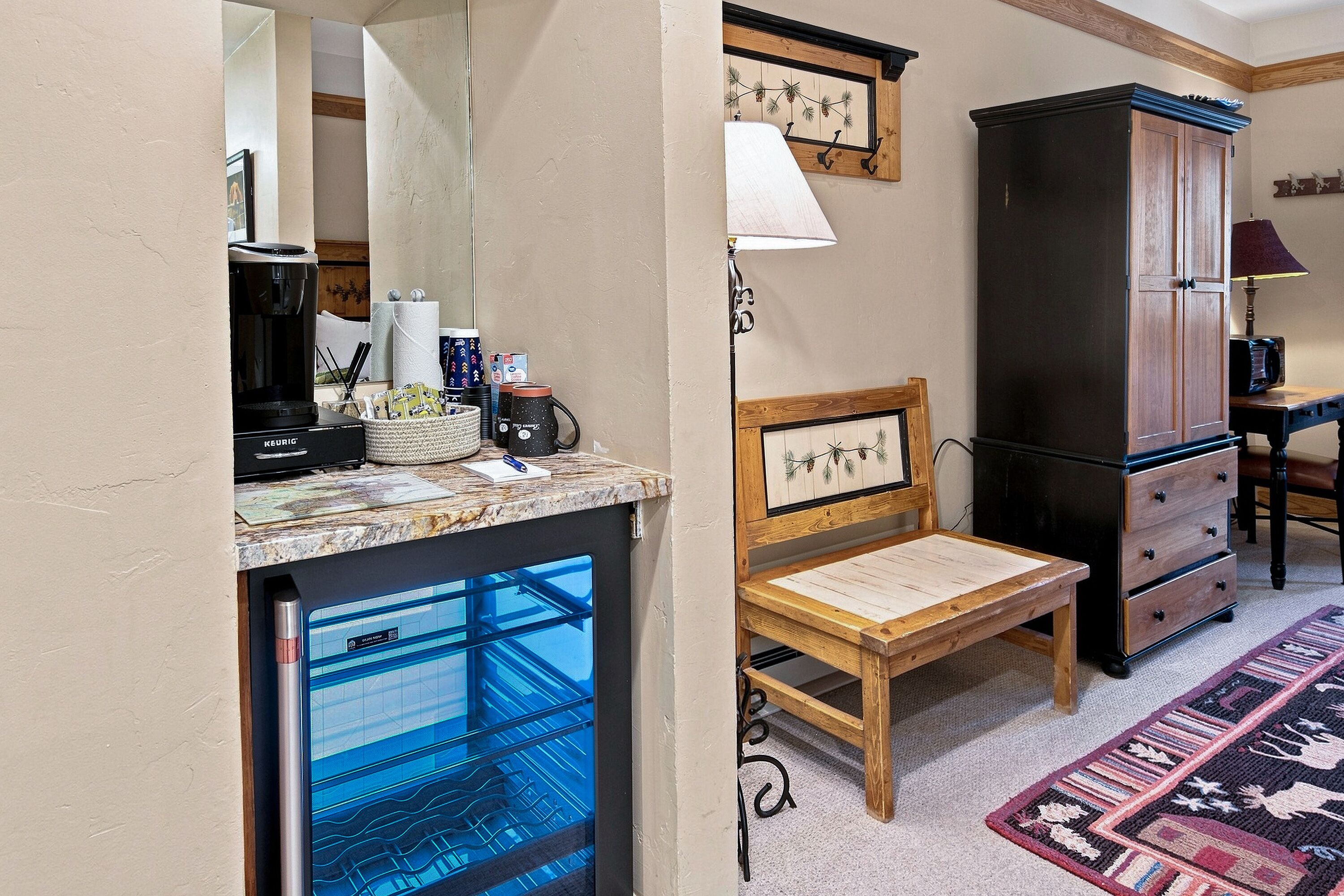 A compact room with a kitchenette, a wooden chair, a cabinet, and a patterned rug.