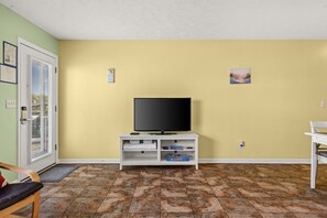 Ein Wohnzimmer mit Fernseher auf einem weißen Schrank, einer Tür mit Fenster und einem Fliesenboden.