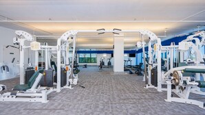 Un gimnasio con diversas máquinas de ejercicio, un amplio ventanal y suelo cubierto de alfombra.