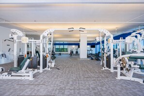 Ein Fitnessraum mit verschiedenen Trainingsgeräten, einem großen Fenster und einem Teppichboden.