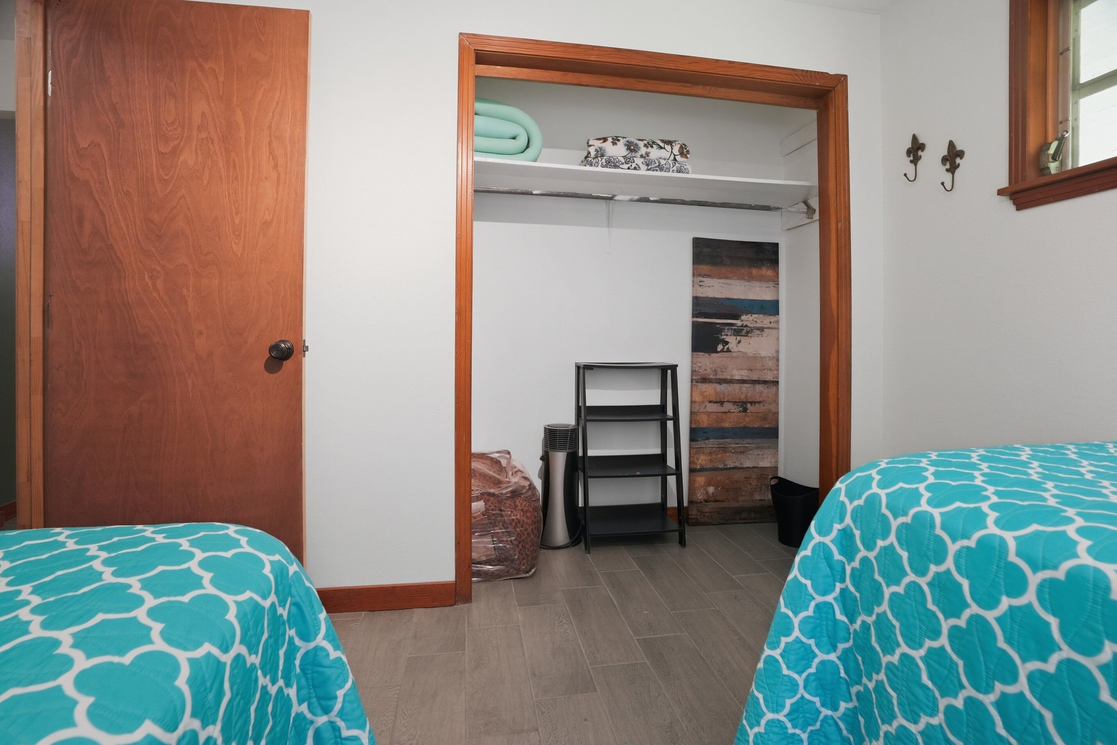 Un dormitorio con dos camas, una puerta de madera, una estantería con objetos y una pared de ladrillo.