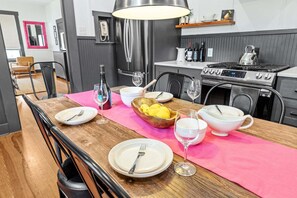 Ein Essbereich mit einem Holztisch, gedeckt für vier Personen, einer rosafarbenen Tischmatte und einer modernen Küche im Hintergrund.