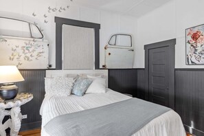 Ein Schlafzimmer mit einem Bett, einem Nachttisch, einer Lampe, einem Spiegel und einer Tür.
