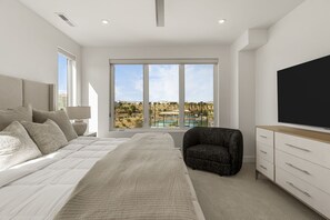 A modern bedroom with a large bed, a chair, a TV, and a view of a pool and landscape. - Courtside Sunsets 5 Bedroom Townhouse (St. George)