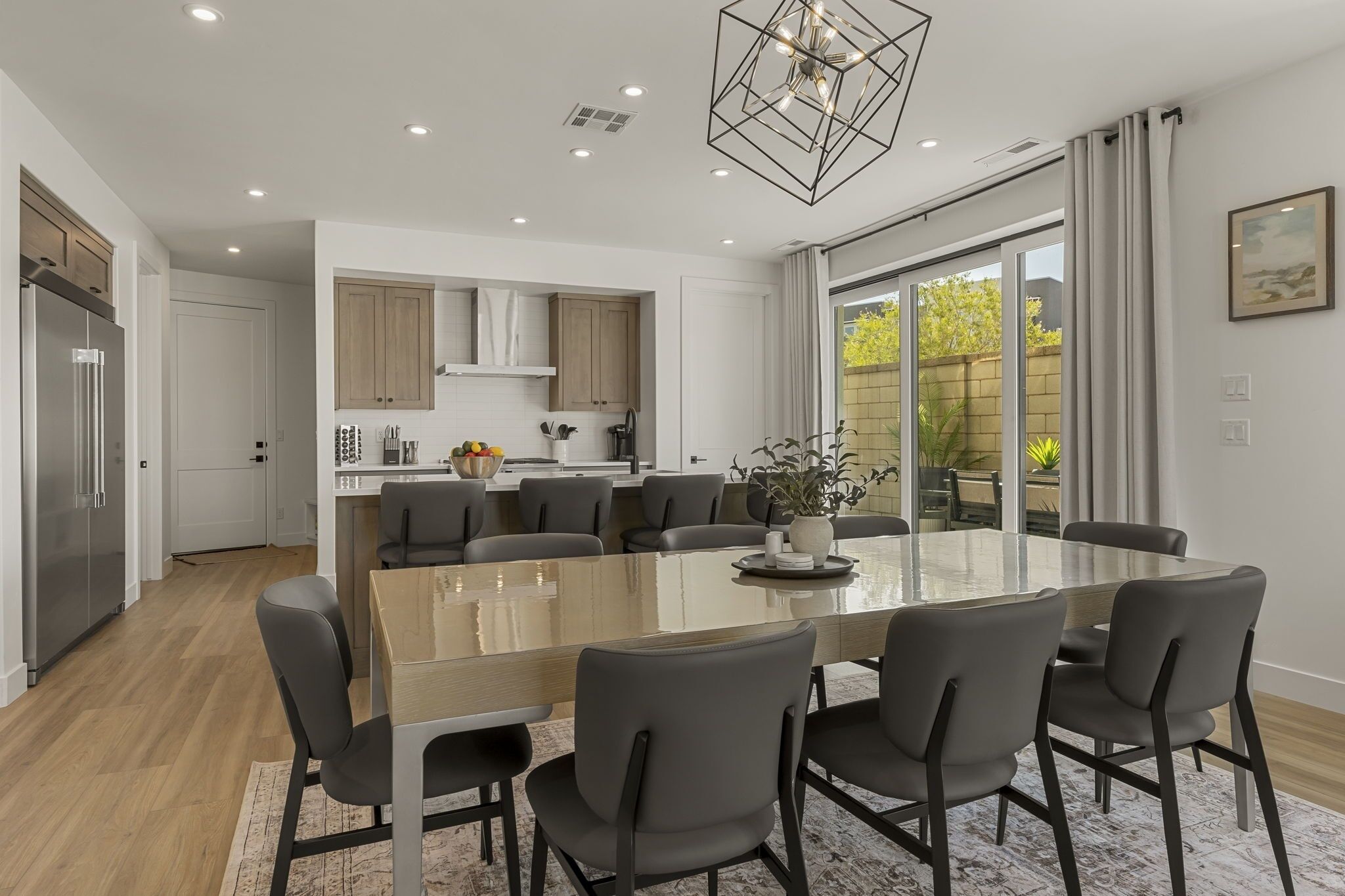 A modern kitchen with a central island, a dining area with a glass table, and a view of the outdoors.