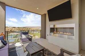 A balcony with a fire pit, seating, and a view of a pool and distant buildings. - Courtside Sunsets 5 Bedroom Townhouse (St. George)