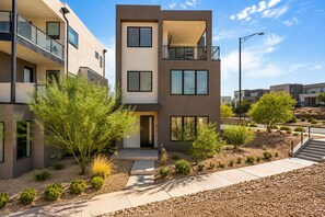 A modern multi-story residential building with balconies, a landscaped garden, and a clear sky. - Courtside Sunsets 5 Bedroom Townhouse (St. George)