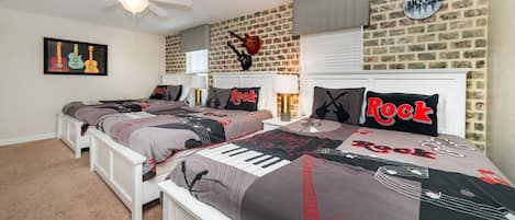 A bedroom with two beds, a brick wall, a ceiling fan, and a wall clock.