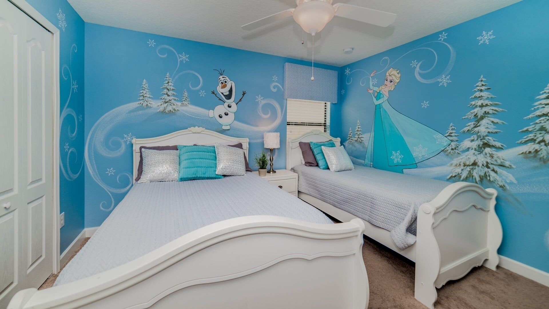 A bedroom with two beds, a ceiling fan, and a wall with winter-themed decorations.