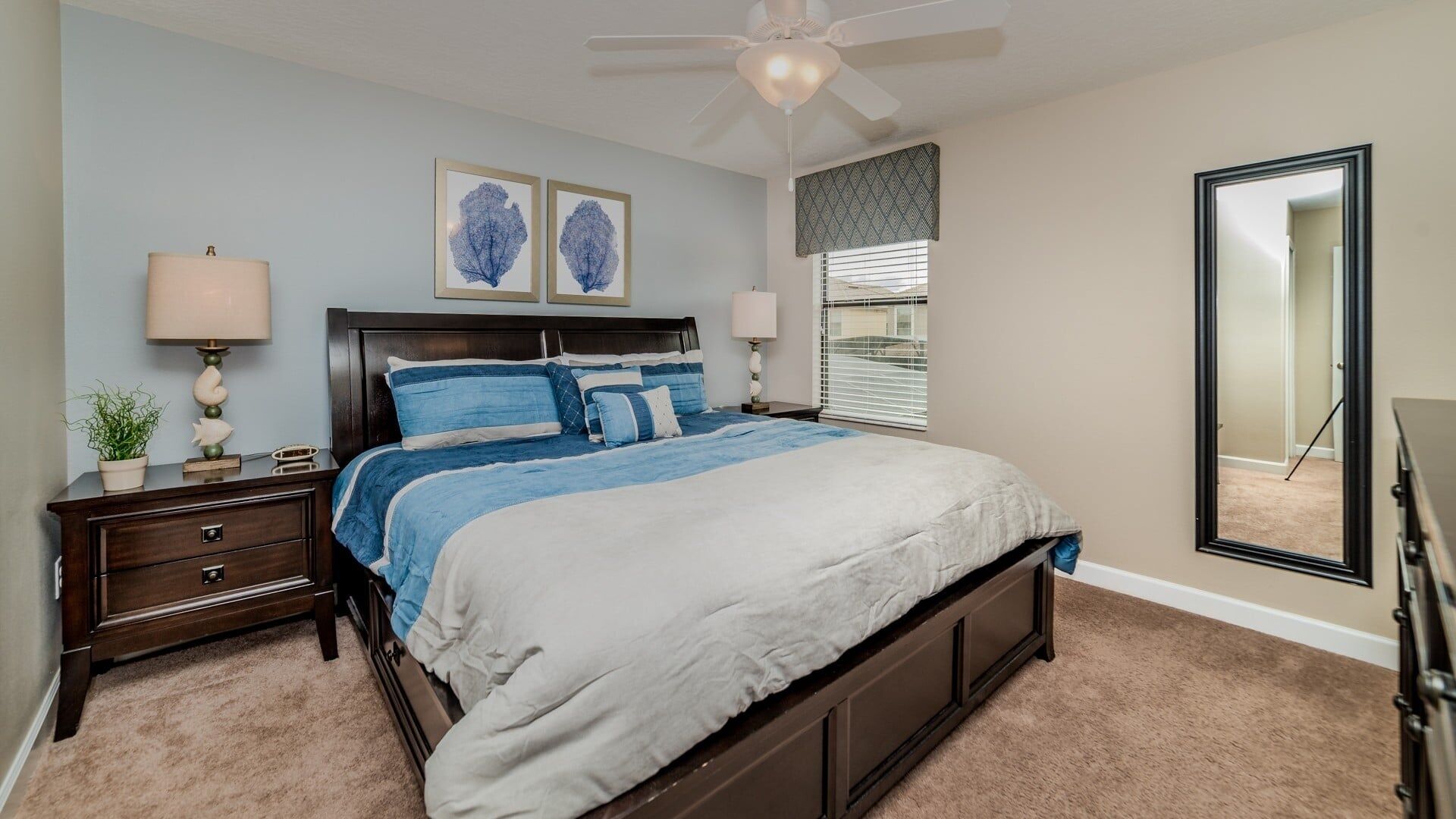 A bedroom with a bed, bedside tables, a ceiling fan, and artwork on the wall.