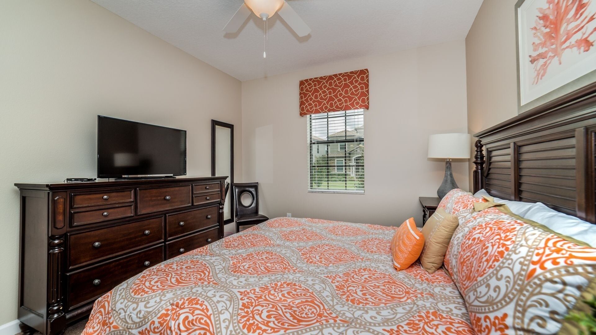 A bedroom with a bed, dresser, television, window, and artwork.